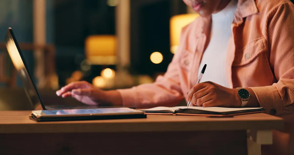 Vrouw schrijft webtekst op notitieboek naast laptop